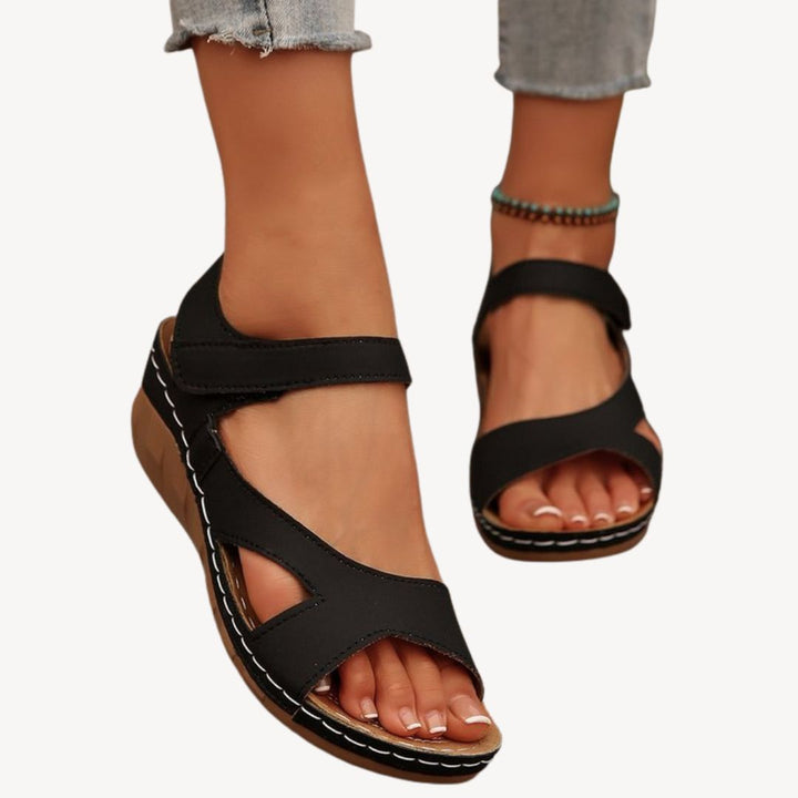 Black women's leather orthopedic sandals with adjustable Velcro straps, low wedge heel, and flexible sole for comfort.