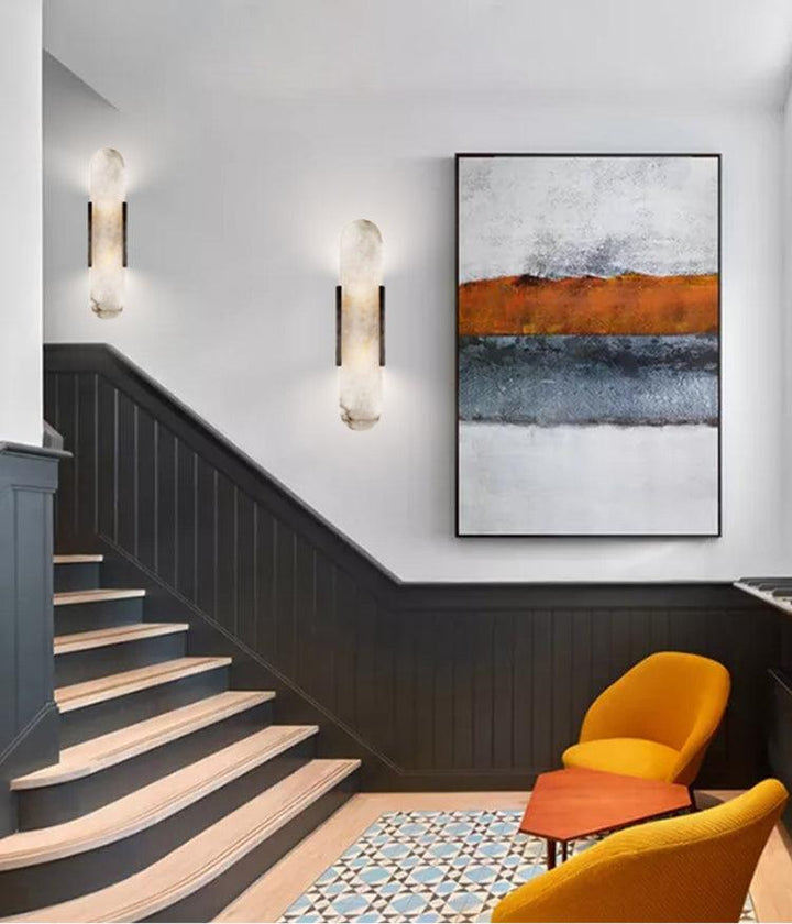 "Modern elongated alabaster wall lamp with metal and brass accents, emits warm glow, suitable for chic interior decor."