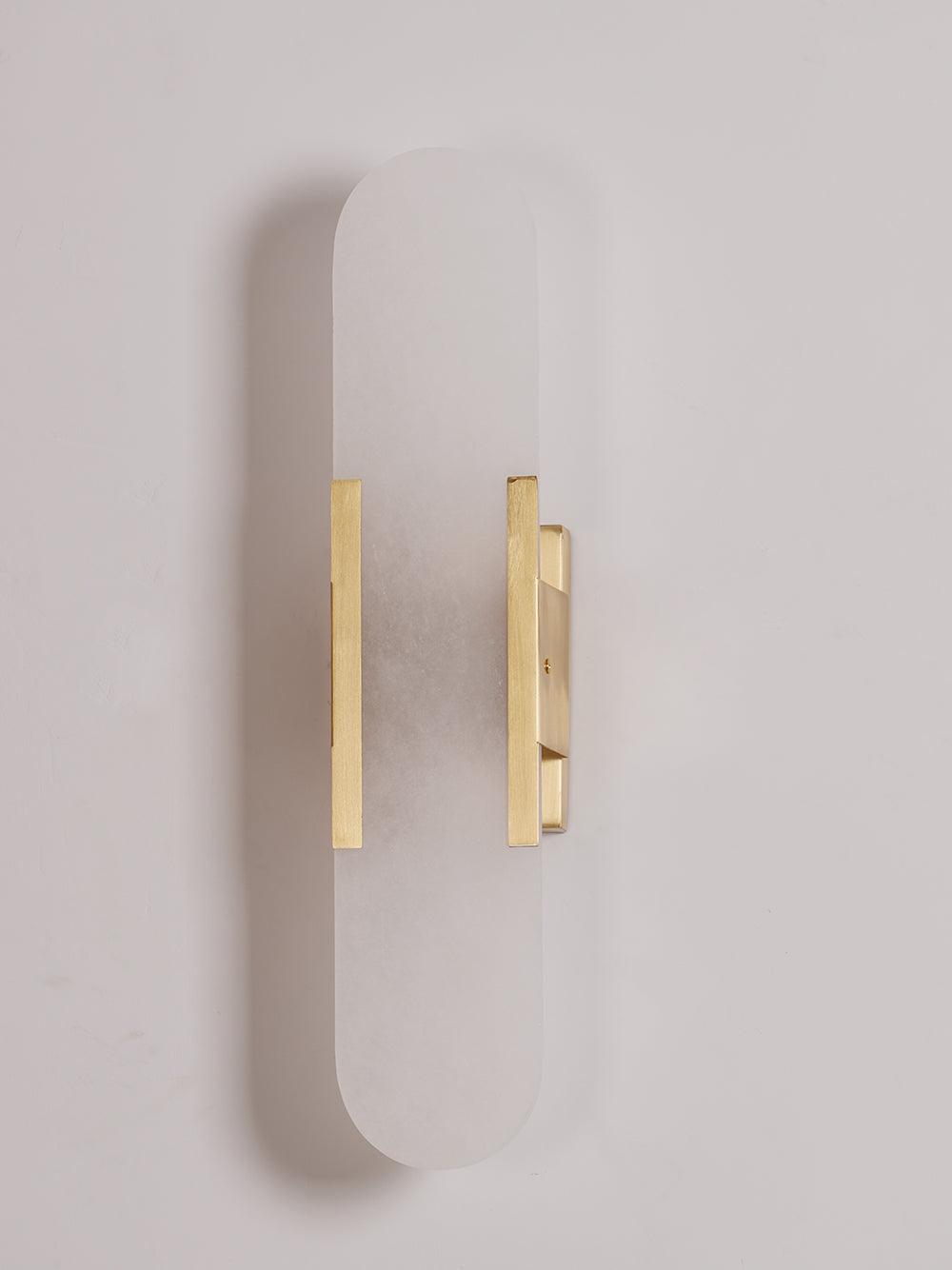 "Modern elongated alabaster wall lamp with metal and brass accents, emits warm glow, suitable for chic interior decor."