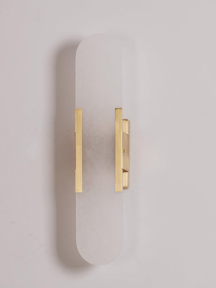 "Modern elongated alabaster wall lamp with metal and brass accents, emits warm glow, suitable for chic interior decor."