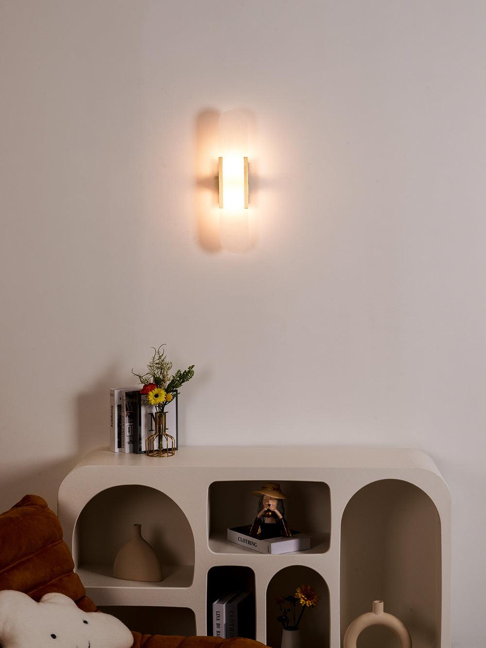 "Modern elongated alabaster wall lamp with metal and brass accents, emits warm glow, suitable for chic interior decor."