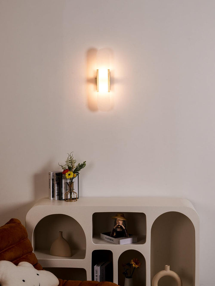 "Modern elongated alabaster wall lamp with metal and brass accents, emits warm glow, suitable for chic interior decor."