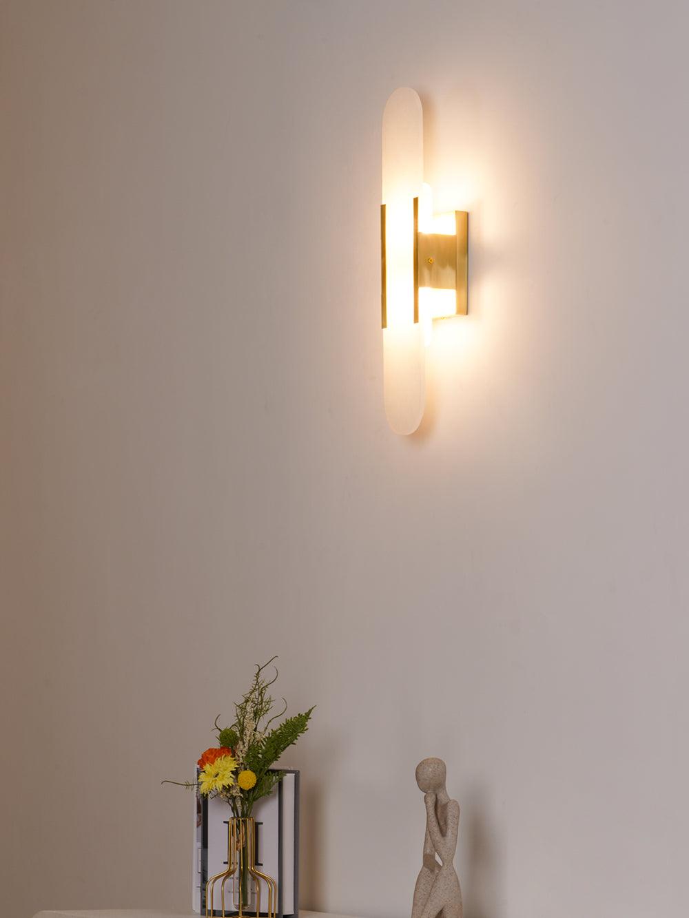 "Modern elongated alabaster wall lamp with metal and brass accents, emits warm glow, suitable for chic interior decor."