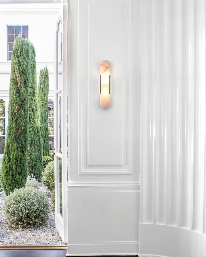 "Modern elongated alabaster wall lamp with metal and brass accents, emits warm glow, suitable for chic interior decor."