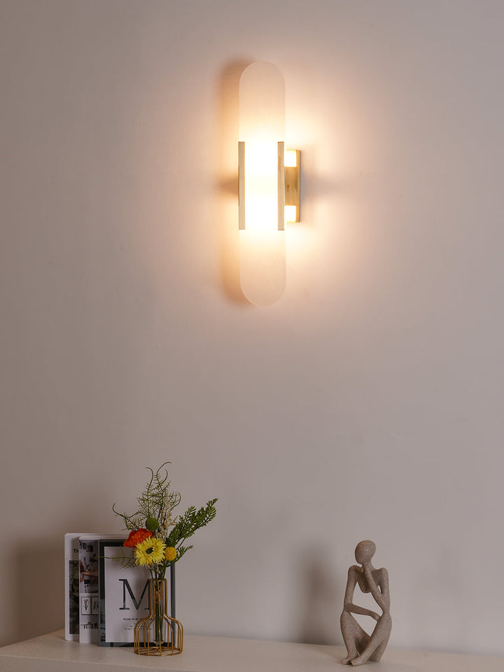 "Modern elongated alabaster wall lamp with metal and brass accents, emits warm glow, suitable for chic interior decor."