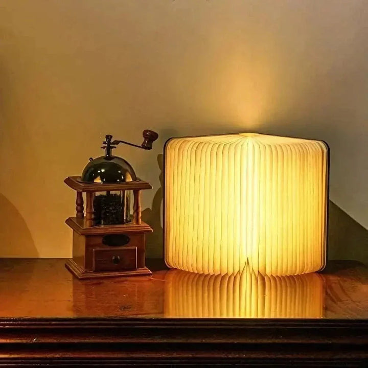 "Elegant foldable LED book lamp, warm white light, 360-degree design, portable for home or travel, wood and paper material."