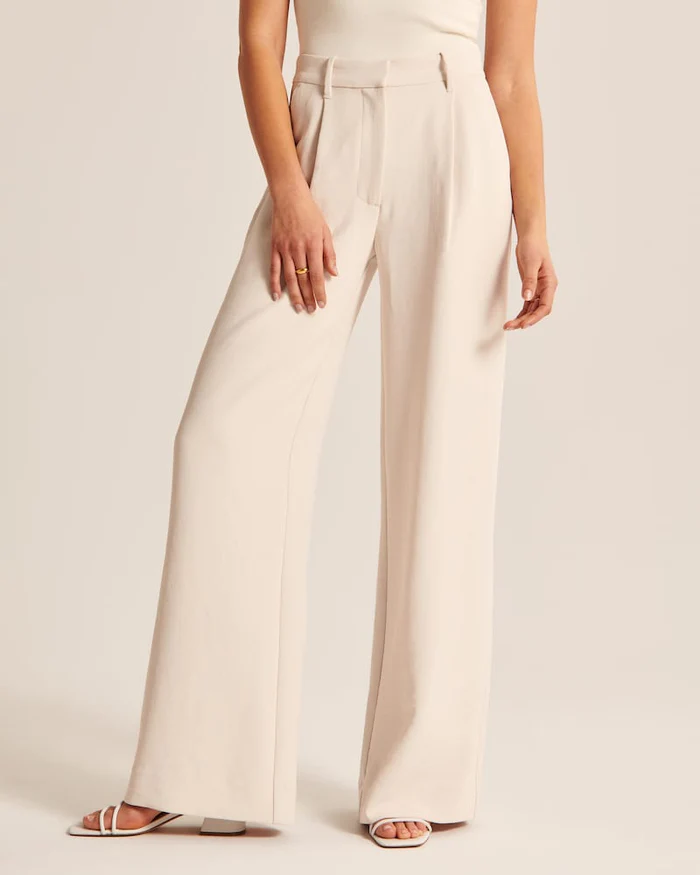 Model wearing women's beige wide-leg tailored trousers, high-waist, elegant style for both formal and casual occasions.