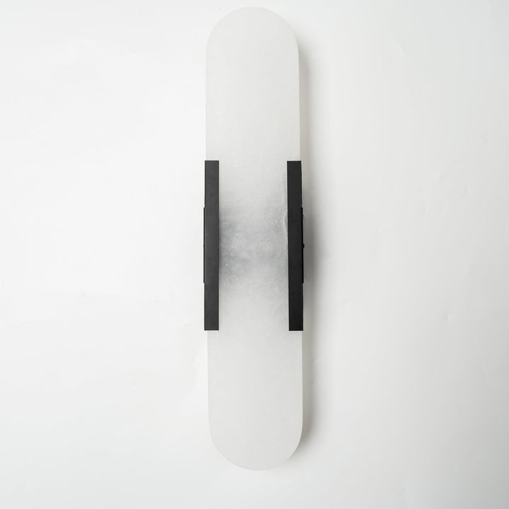 "Modern elongated alabaster wall lamp with metal and brass accents, emits warm glow, suitable for chic interior decor."