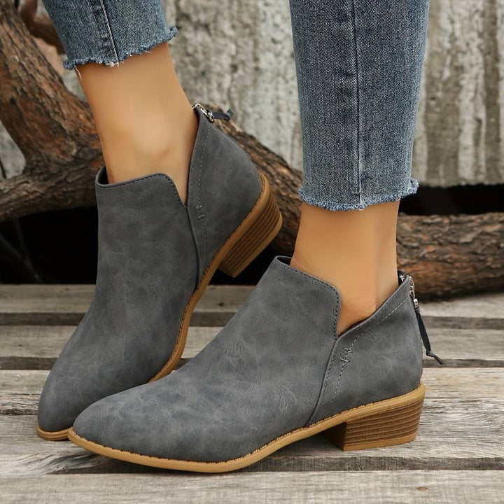Side view of women's suede ankle boots with low block heel, pointed toe, and back zip, showcasing elegant and chic design.